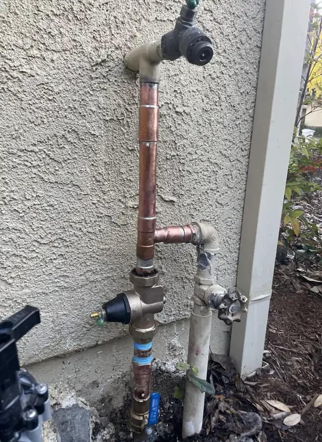 New copper water line with a pressure regulator and hose bib on a stucco exterior wall