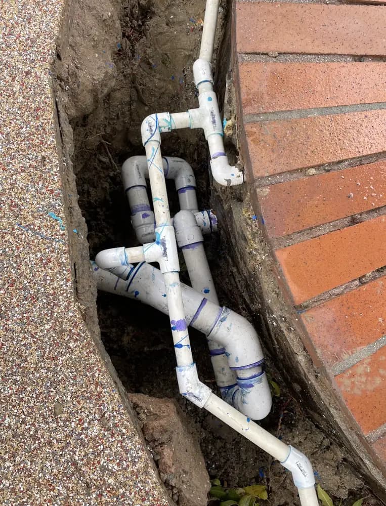 New PVC pool lines laid in an open trench beside a brick-edged spa