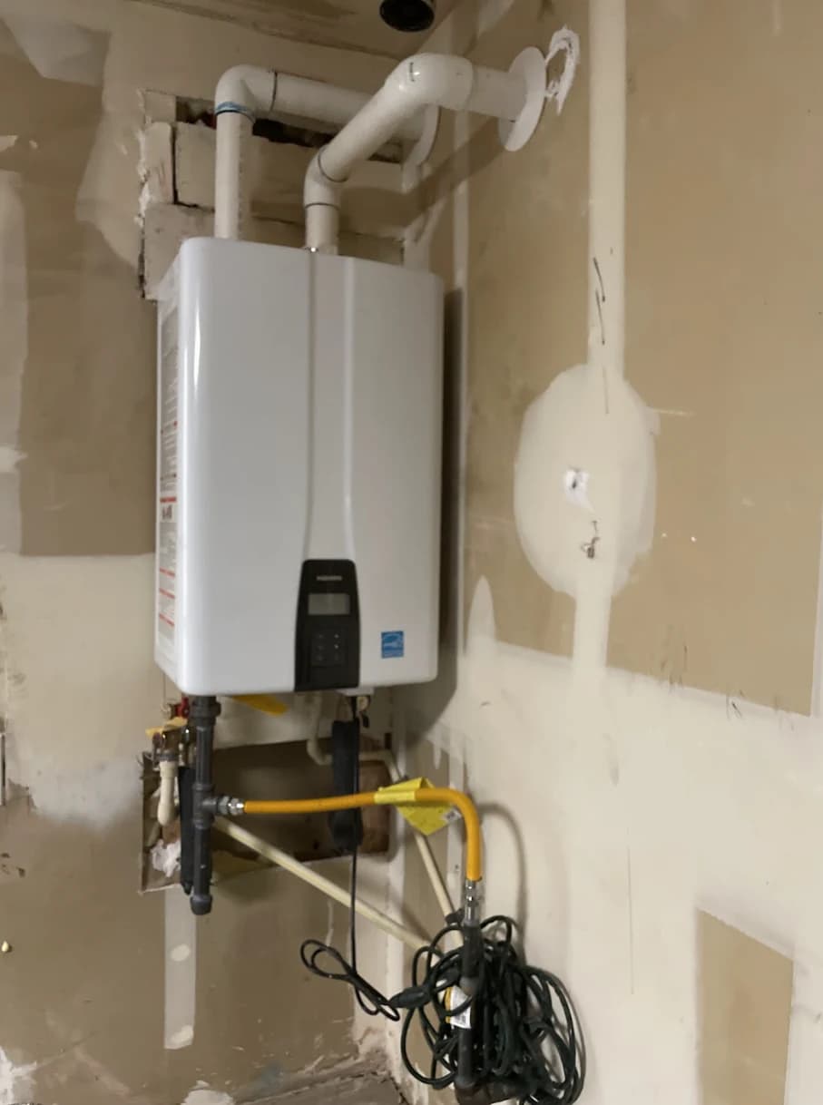 Wall-mounted tankless water heater with PVC vent piping and patched drywall