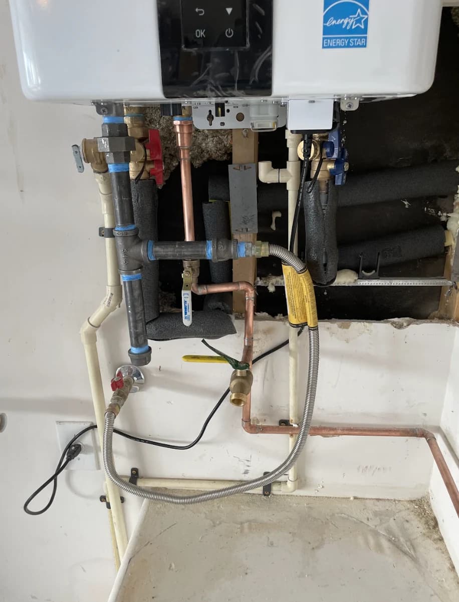 Tankless water heater with new isolation valves, copper lines and a yellow gas connector, wall opened below