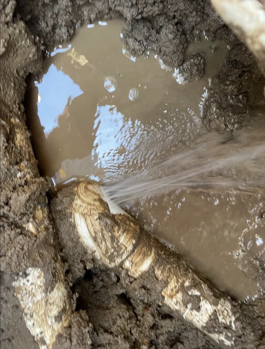 Water spraying from a broken pipe in a muddy excavation